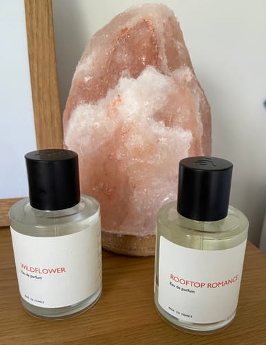 Customer's Rooftop Romance and Wildflower perfume bottles sitting side-by-side on a wooden surface.