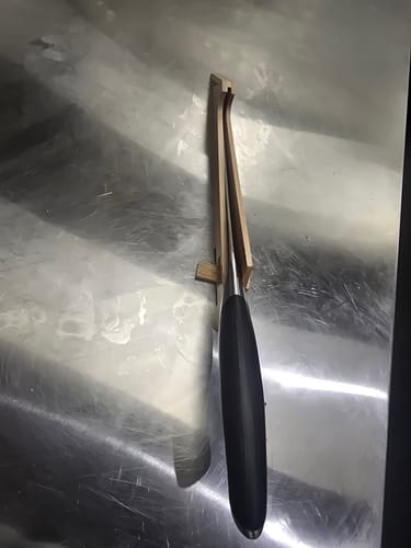 Customer's 7" fillet knife with a black handle, resting inside its wooden sheath on a counter.