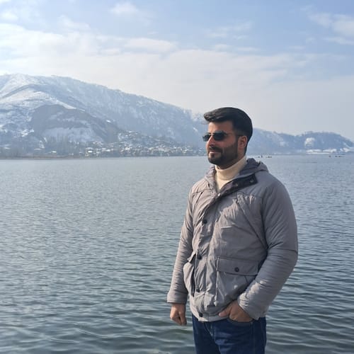 Reviewer wearing the Evoke Grey Rimless Sunglasses while standing outdoors by a lake with snowy mountains in the background.