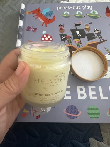 Reviewer holds an open jar of yellow Melvory Hemp Seed Butter in their hand.