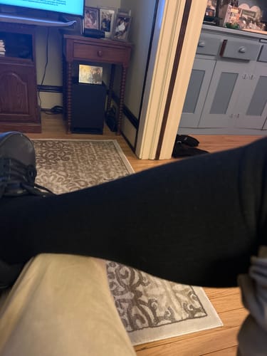 Reviewer's leg propped up to show the fit of the black Performance Eucalyptus Compression Socks in a living room.
