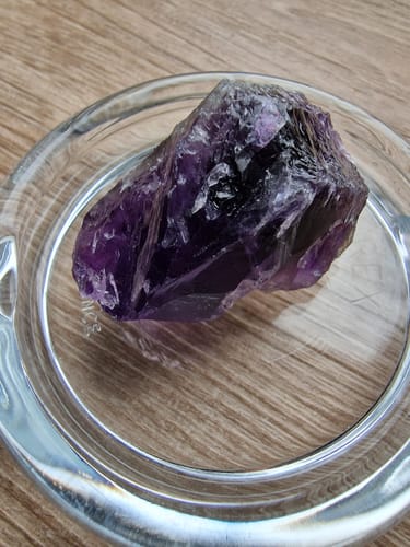 Photo d'un client montrant une pierre d'Améthyste brute et violet foncé dans un petit plat en verre sur une table.