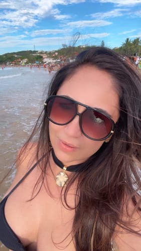Close-up de uma cliente na praia usando os Óculos Veneza pretos com lentes em degradê.