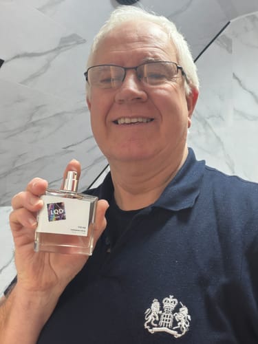 A happy customer holds up their bottle of For Him Pheromone Perfume in a bathroom setting.
