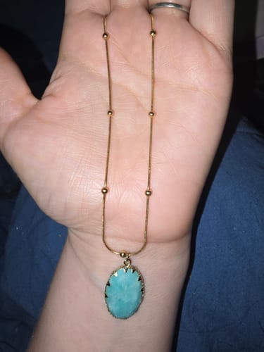 Customer holding a delicate gold necklace with an oval, light-blue stone from their AuraBloom Subscription Box.