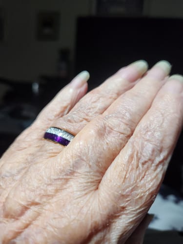 A reviewer's hand wearing the Guardian ring, showing its purple lapis lazuli and textured meteorite inlays.