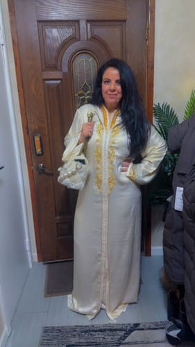 Reviewer standing indoors wearing the full-length, ivory Jellaba Aranel Pearl with gold embroidery.