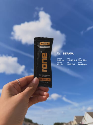 Customer holding a packet of SuperCharged Honey against a blue sky with their Strava running stats overlaid.
