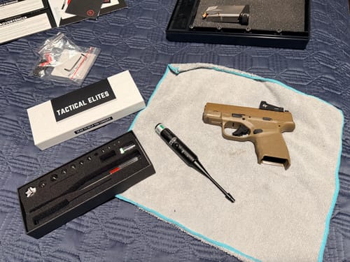 Customer's Site Right™ 2.0 - Boresighter kit laid out with a handgun and accessories on a bed.