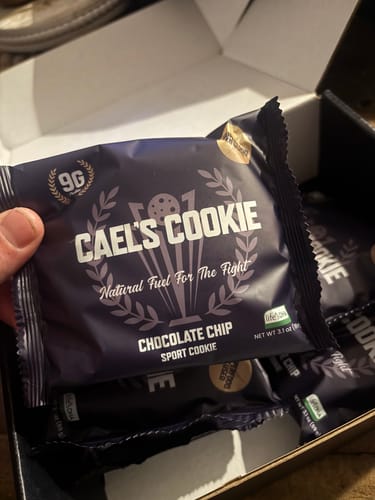 Customer holding a Cael's Cookie Chocolate Chip in its purple wrapper, taken from a full box.