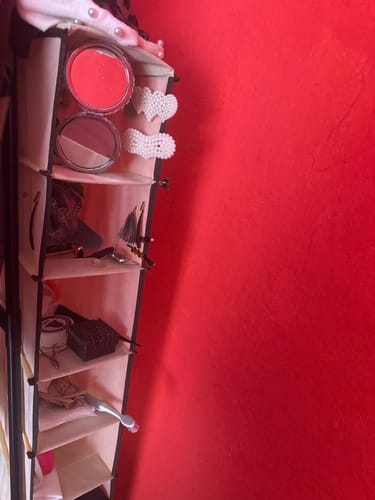 Cliente usando la zapatera colgante color crema para guardar maquillaje y accesorios contra una pared roja.