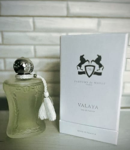 Recensore mostra il flacone di profumo VALAYA Parfums de Marly con la sua elegante scatola bianca su un tavolo.