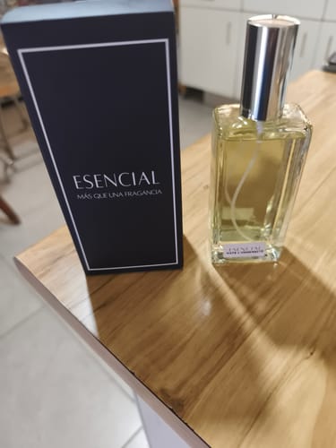 Un cliente muestra el perfume Esencial H275 en su frasco de vidrio junto a su caja negra sobre una mesa.