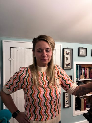 A reviewer shows the fit of the colorful Michaela Wavy Striped Sweater Top in a room.