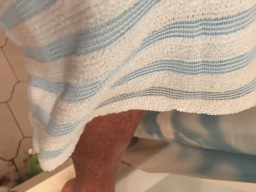 Közelkép: A vásárló a csíkos Silkura testradírozó törölközőt a lábán használja.