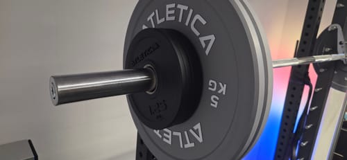 Kunde zeigt eine graue 5 kg Color Bumper Plate in Nahaufnahme auf einer Langhantel.