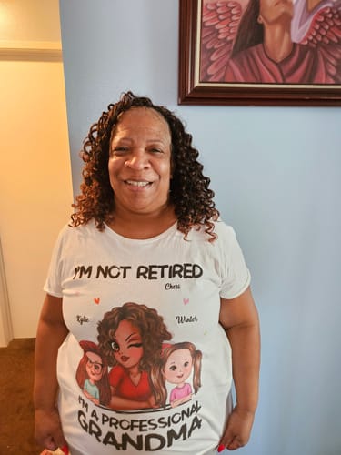A happy reviewer smiles while wearing her white personalized "I'm Not Retired I'm A Professional Grandma" shirt.