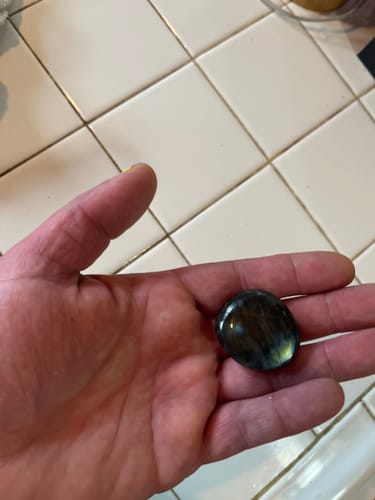 Reviewer holding a polished, dark crystal with an iridescent sheen in the palm of their hand.