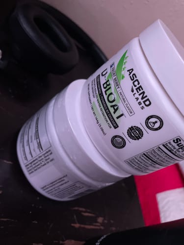 Reviewer's two stacked white tubs of D-BLOAT powder on a desk.