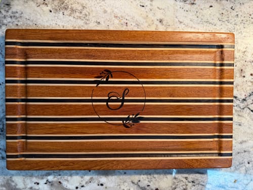Customer's striped wooden cutting board with a sharp, burnt-in monogram created after using the Wood Pre-Treatment.