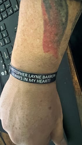 Customer wearing their black customized bracelet with the text 'Christopher Layne Barron' and 'Always in my heart!'.