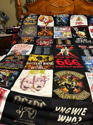 Customer's Premium T Shirt Quilt made from rock concert t-shirts, spread flat across a wooden bed.