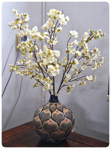 Recensent toont de witte Zijden Bloesems in een grote, decoratieve vaas op een houten tafel.