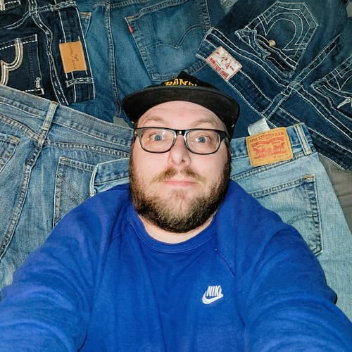 Reviewer lying on a pile of various blue jeans from their Wrangler Jeans bale purchase.