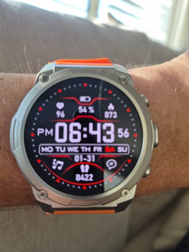 Close-up of a reviewer's smartwatch on their wrist, with the digital face showing 54% battery life.