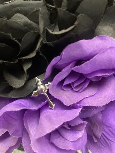Close-up of a customer's silver Down Your Throat Ring resting on purple and black flowers.