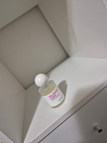 A customer's bottle of Majestic Aura perfume with a white cap, sitting in the corner of a white shelf.