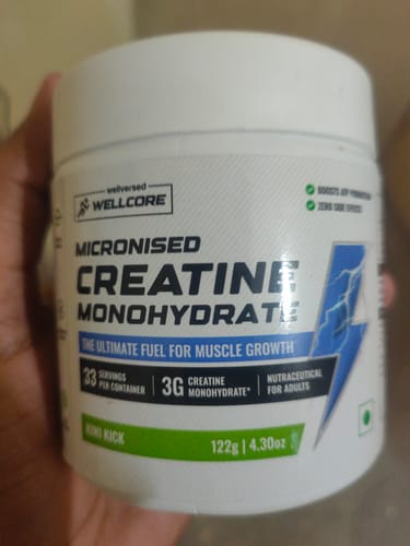 Customer holding the white tub of Wellcore Pure Micronised Creatine Monohydrate in the Kiwi Kick flavor.