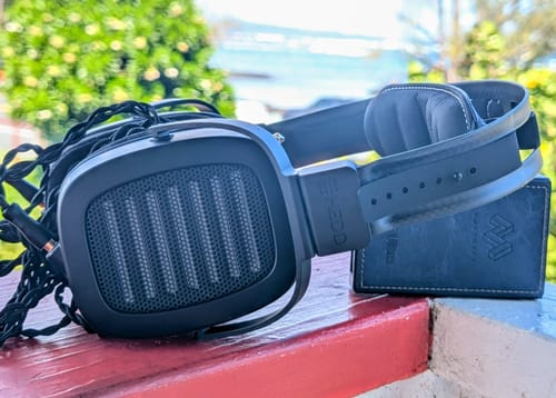 Reviewer's black HEDDphone TWO GT headphones resting on a red ledge outdoors, showing the earcup grille and headband.
