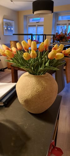 Klant toont de ronde, beige Arda vaas gevuld met een bos gele tulpen op een tafel.