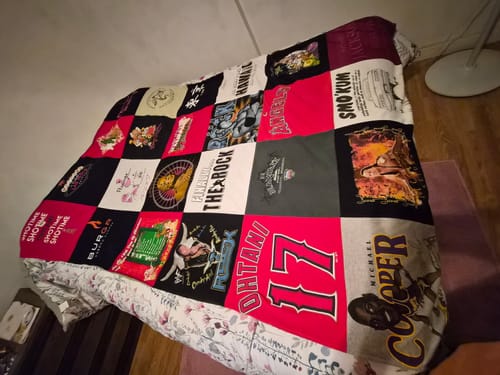 Customer's Premium T Shirt Quilt made from a colorful patchwork of t-shirts, spread across a bed.