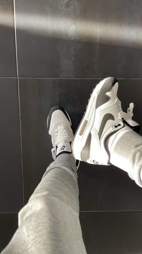 Recensent draagt de Nike Air Max 1 White Black schoenen, van bovenaf gezien op een donkere tegelvloer.