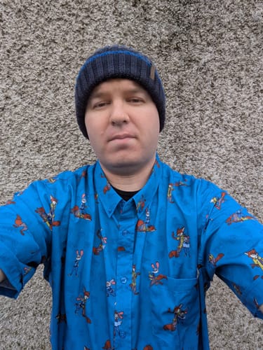 Reviewer wearing a beanie and the bright blue Disney's Zootopia "Paw & Order" short sleeve shirt against a textured wall.