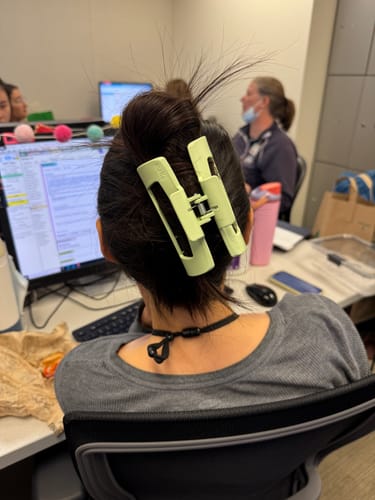 Reviewer at a desk with their dark hair held up in a messy bun by a large, light green Mello claw clip.