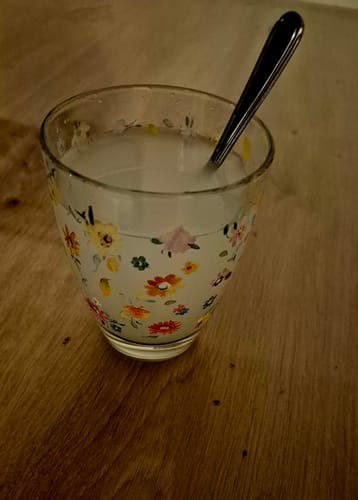 Ein Kunde zeigt das zubereitete OMNi-BiOTiC SR-9 in einem geblümten Glas mit Löffel.