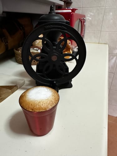 Customer's Nanyang Kopi Roast prepared in a red cup with a frothy top, shown next to a coffee grinder.
