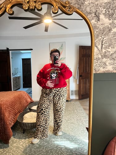 Customer wearing the wide-leg, leopard print For The Taking Pants, styled casually with a red sweatshirt in a bedroom.