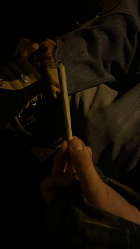 Close-up of a customer holding a lit ROLLZ THCA Pre-Roll in a dark setting.