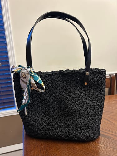 Customer's completed black Aveline crochet Shoulder Bag with a decorative scarf tied to the handle, on a wooden table.