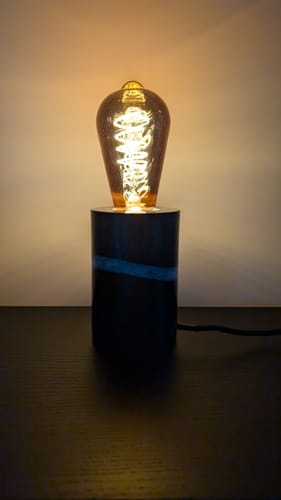 Recensent toont de ingeschakelde Marissa tafellamp op een donkere tafel, die een warm licht uitstraalt.