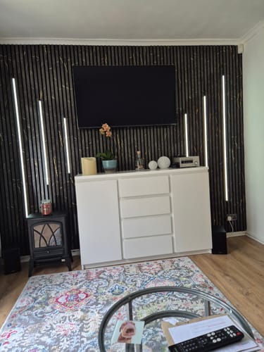 Customer's Wall Panel LED Lighting Strip Kit installed vertically on a dark slatted wall, glowing brightly in a living room.