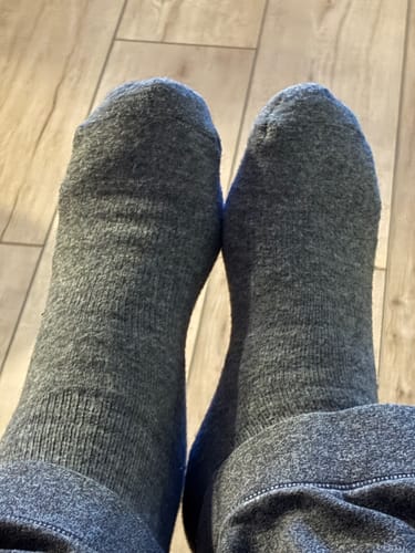 A reviewer's feet wearing a pair of gray Men's Alpaca Socks.