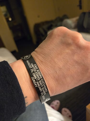 Close-up of a reviewer wearing a black customized memorial bracelet on their wrist with personalized text visible.