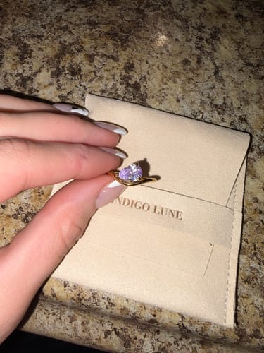Close-up of a customer holding the Pia Birthstone Ring with a light purple stone over its pouch.