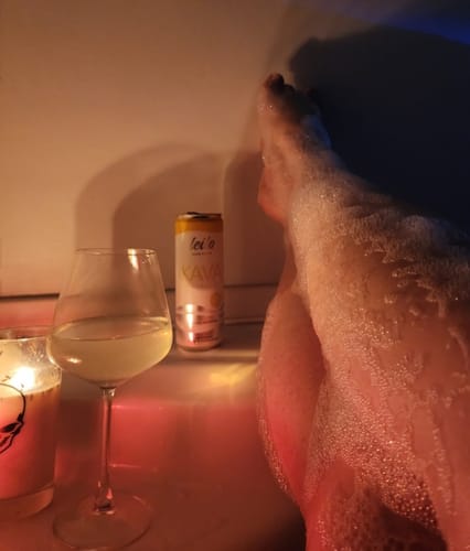 A customer enjoys a relaxing, candlelit bubble bath with a can of Leilo Kava Tonic resting on the tub's edge.