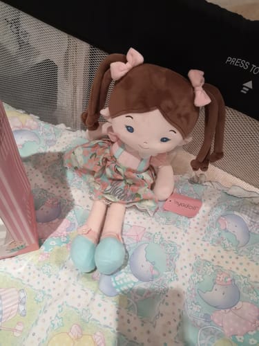 Customer's Personalized Meadow Girl doll with a charming floral dress and brown pigtails, sitting in a crib.